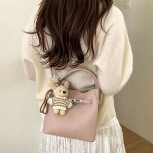 Pink lychee leather bucket bag with teddy bear charm shown on a casual chic outfit