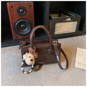 Detailed close-up of brown patent leather handbag with cartoon embossing and a teddy bear charm