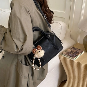 Close-up of black retro tote bag with teddy bear charm on a khaki trench coat background