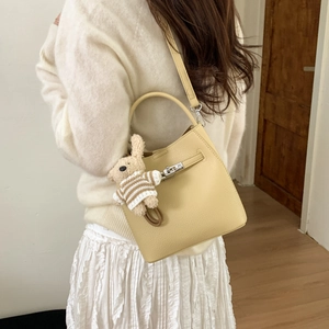 Close-up of creamy yellow leather bucket bag featuring a rotating metal clasp and bear charm