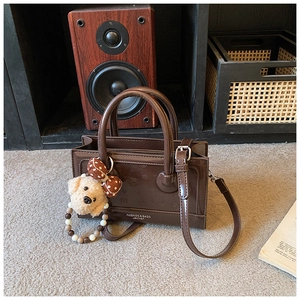 Detail of dark brown leather handbag featuring a plush puppy charm and embossed animal pattern