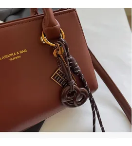 Close-up of brown faux leather bag featuring a gold logo and a unique abacus charm detail