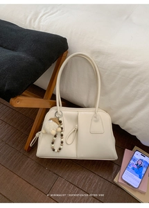 Detail view of cream underarm bag featuring a trendy plush charm and wooden beads