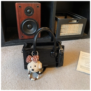Close-up of black glossy crossbody bag with embossed smiley and plush dog pendant