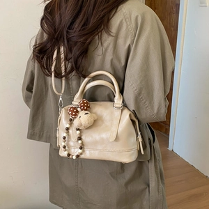 Detailed view of cream Boston style handbag with plush bear charm on adjustable shoulder strap