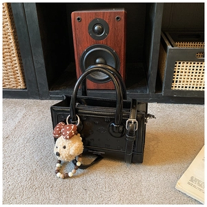 Detail view of black embossed leather crossbody bag with cute plush puppy charm