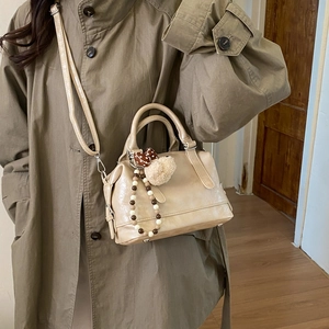 Detail of beige Boston bag with decorative charms and adjustable shoulder strap worn by model