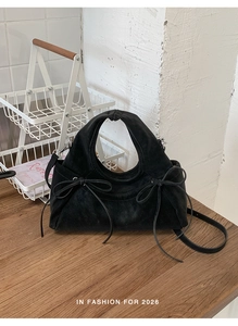 Dettaglio della borsa in pelle scamosciata nera con fiocchi decorativi e tracolla sottile
