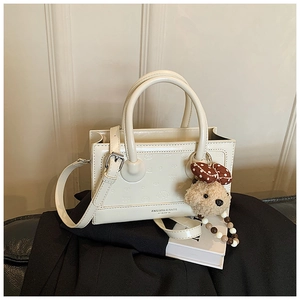 Detail of off-white leather handbag featuring cartoon embossed patterns and plush puppy charm
