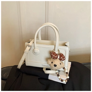 Detail of cream leather handbag with embossed texture, fashion logo and cute bear charm