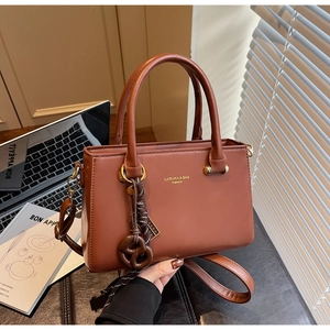 Close-up of brown faux leather handbag with metal logo and knotted decorative charm