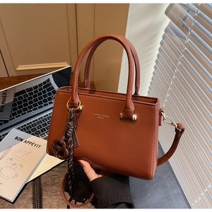 Detailed view of caramel box handbag with gold logo, woven knot charm and detachable strap