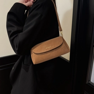 Gros plan du sac en daim marron montrant le logo en métal et la texture mate