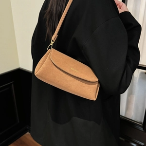 Détail du sac à bandoulière rectangulaire en daim beige avec logo doré sur blazer noir