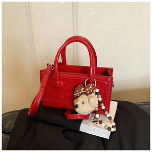 Detail of red structured patent leather handbag with teddy bear charm and beaded strap
