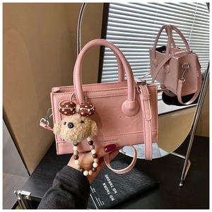 Detail of pink patent leather handbag with embossed heart patterns and plush bear charm