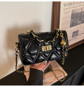 Detail of black quilted patent leather bag with gold chain strap and spherical charm