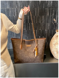 Detail of a large brown tote bag with beaded charm and gold Carolmanti logo plaque