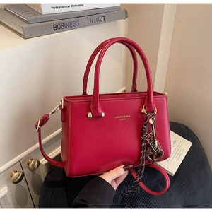 Detail view of red PU leather handbag with gold lettering and decorative bag charm