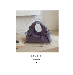 Detail of lavender leather handbag with decorative bows on a marble table with a book