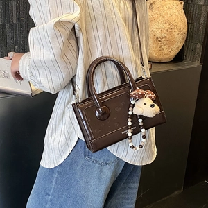Detail of dark brown glossy leather handbag with cute plush puppy and beaded accessories