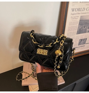 Detail of black glossy patent leather crossbody bag with quilted pattern and gold chain