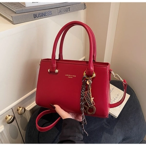 Detail of red PU leather handbag with golden abacus charm and brand logo on a blue stool