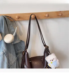 Détail d'un sac cabas en cuir marron foncé suspendu à un crochet avec un ours en peluche