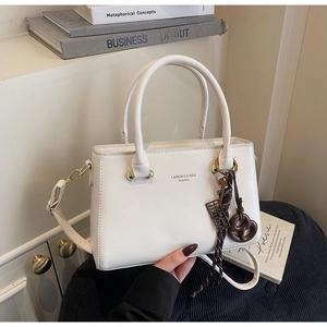 Detail view of cream leather crossbody bag with gold lettering and brown knot charm