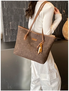 Close-up of brown tote bag featuring embossed bear patterns and wooden bead tassel detail
