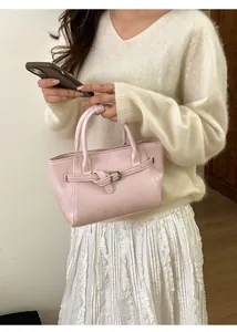 Détail du sac à main en cuir rose avec boucle sur un mannequin portant un pull blanc