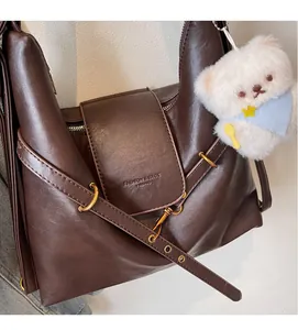 Détail du sac cabas en cuir marron avec logo embossé et breloque ours en peluche blanc