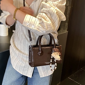 Detail of dark brown glossy leather handbag with cute teddy bear charm and top handles