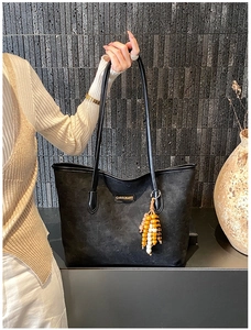 Detailed close-up of a black embossed tote bag with a beaded tassel and metal logo plate
