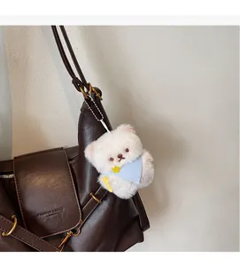Détail d'un ours en peluche avec bavoir bleu et cuillère suspendu à un sac en cuir marron