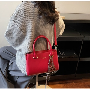 Detail of red matte leather square bag with pretzel charm shown on shoulder