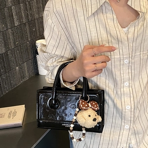 Detail of black patent leather small square bag with embossed dog and plush charm
