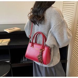 Detail of red PU leather small square bag with golden hardware and woven charm pendant