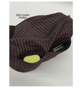 Detail of the side pocket on a plaid shoulder bag showing a phone and earphones inside