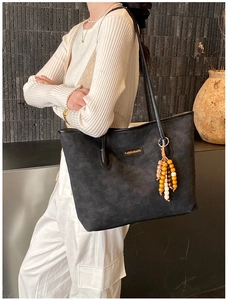 Detail of a black large tote bag with gold logo and colorful ethnic bead charm
