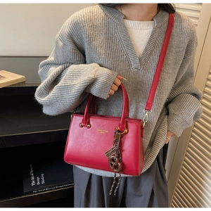 Detail of red synthetic leather handbag with gold logo and stylish decorative pendant