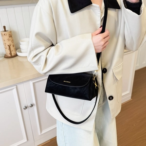 Détail du petit sac bandoulière noir brillant avec boucle dorée porté par un mannequin