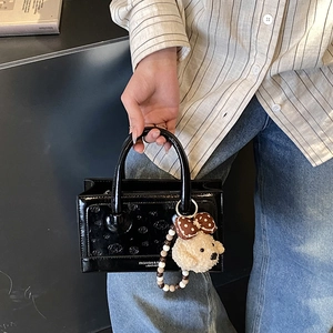Close-up of black patent leather handbag with plush dog charm and fashion text detail