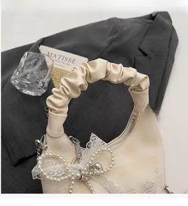 Detail of cream plaid handbag with lace pearl bow and embroidered stars on textured fabric