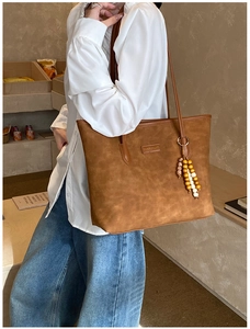 Brown suede tote bag with fringe charm shown on a model in a cozy cafe setting