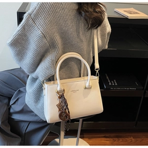 Detail of white leather crossbody bag with stylish cookie charm and shoulder strap