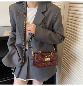 Detail view of burgundy quilted chain bag with gold hardware worn on a grey suit jacket