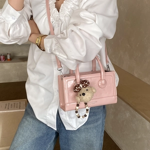 Close-up of pink glossy square handbag with heart embossing and cute bear charm