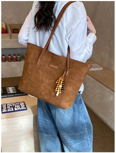 Brown tote bag with embossed pattern, gold logo, and wooden bead tassel detail on handle