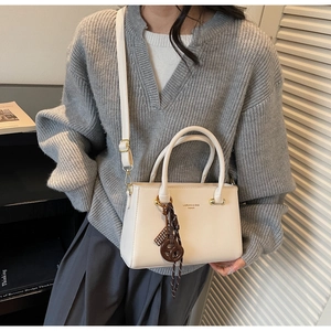 Detailed view of creamy white crossbody bag with gold lettering and decorative pendant
